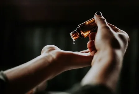 Wellness oil on hands in the GRANDSPA A hand holds a small bottle of oil above an open palm, with one drop falling onto the skin.